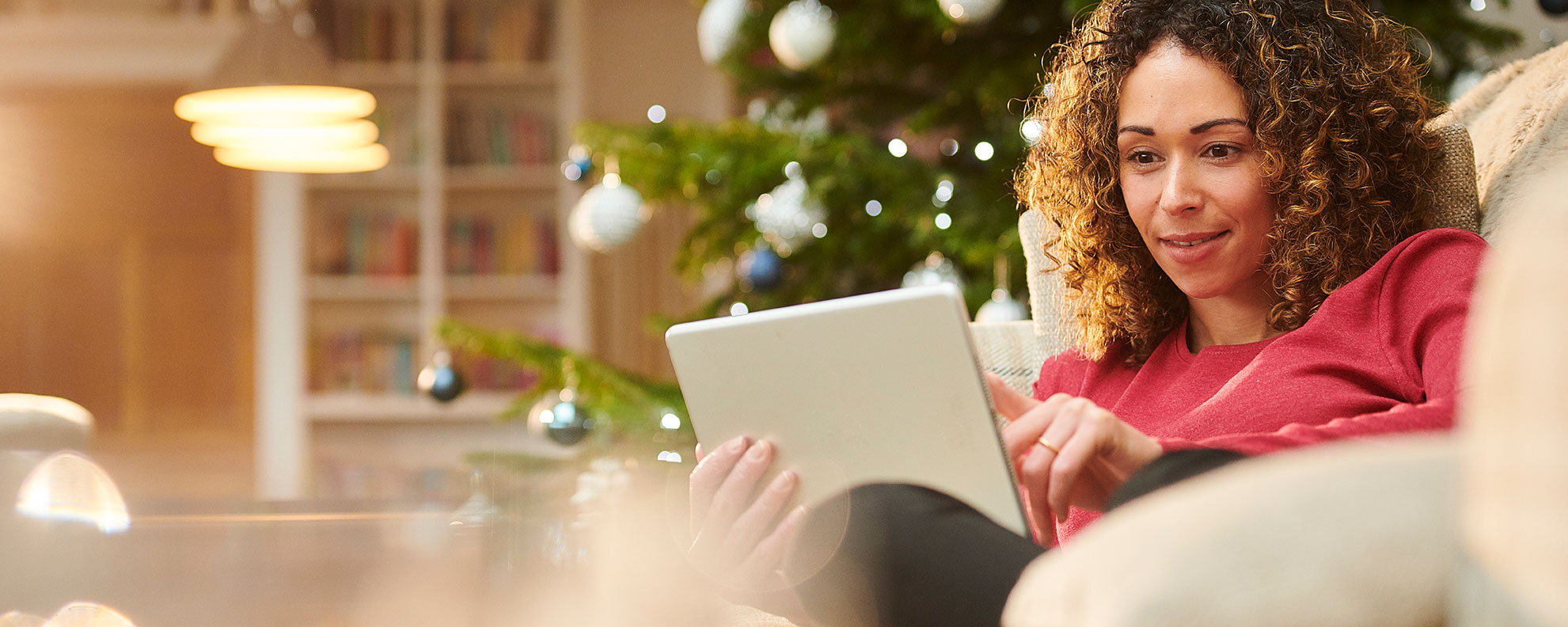 woman on couch in front of christmas tree shopping on tablet