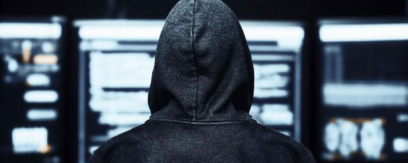 Cybercriminal in hoodie looking at monitors